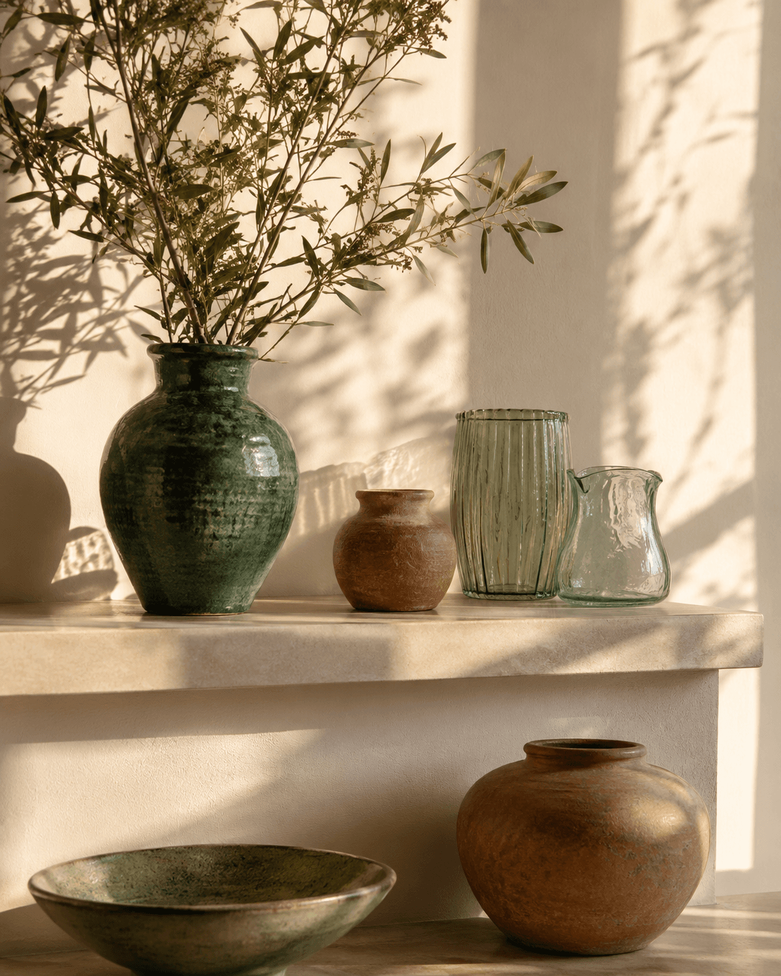 Vases and shelf riser casting botanical shadows on a cream wall