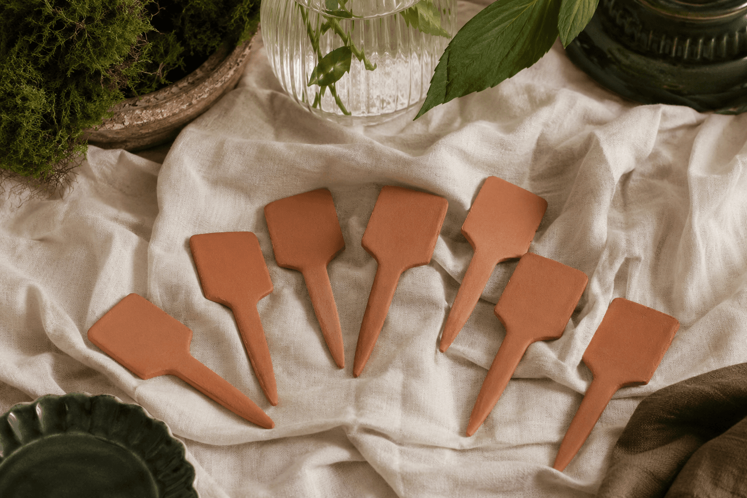 Eight blank terracotta plant markers on cream linen
